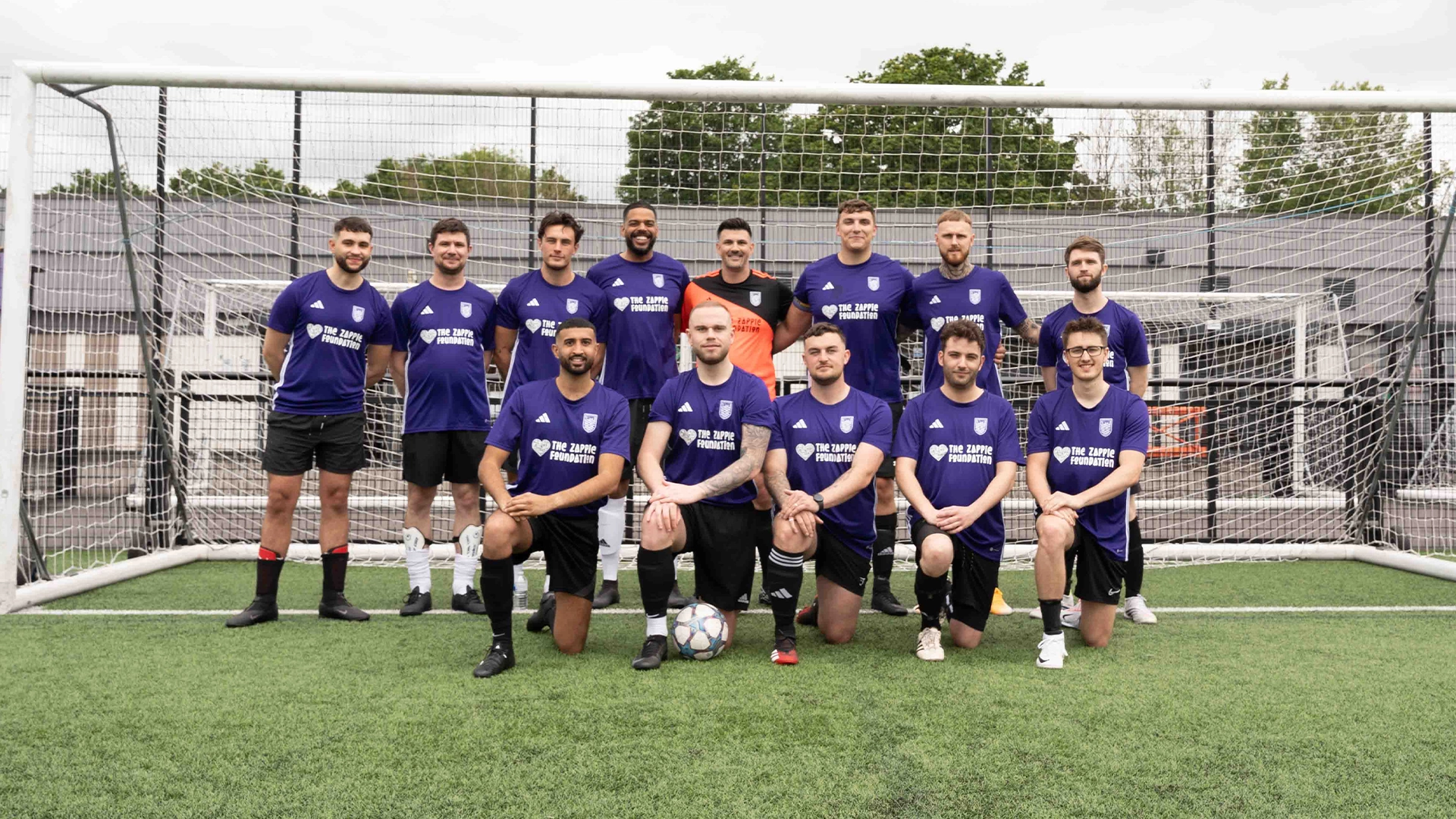 A football team in purple Zappie Foundation shirts posing in front of a goal at Coupe de Zap 2024